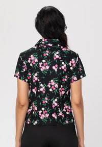 Chemise noire à manches courtes avec un motif floral de tulipes roses et de feuilles vertes. Texture lisse avec un col et une coupe courte.