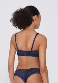 Světlonámořnická krajková podprsenka a odpovídající thong s vlnitými okraji, tenkými nastavitelnými ramínky a zapínáním na háček, která vykazuje jemný květinový vzor.