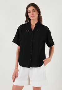 Black short-sleeve blouse with a mandarin collar. Features floral embroidery on sleeves and front, and front button closure.