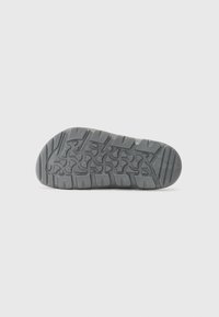 Grå gummisåle med et teksturert mønster med spor og riller for trekkraft. Rundtå og flat hældesign.
