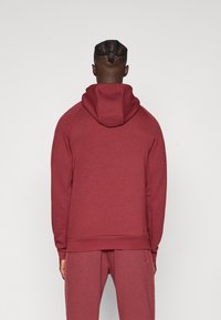 Bordeauxroter Kapuzenpullover mit lockerer Passform, weichem Material und Raglanärmeln. Verfügt über ein schlichtes Design und eine geräumige Kapuze.