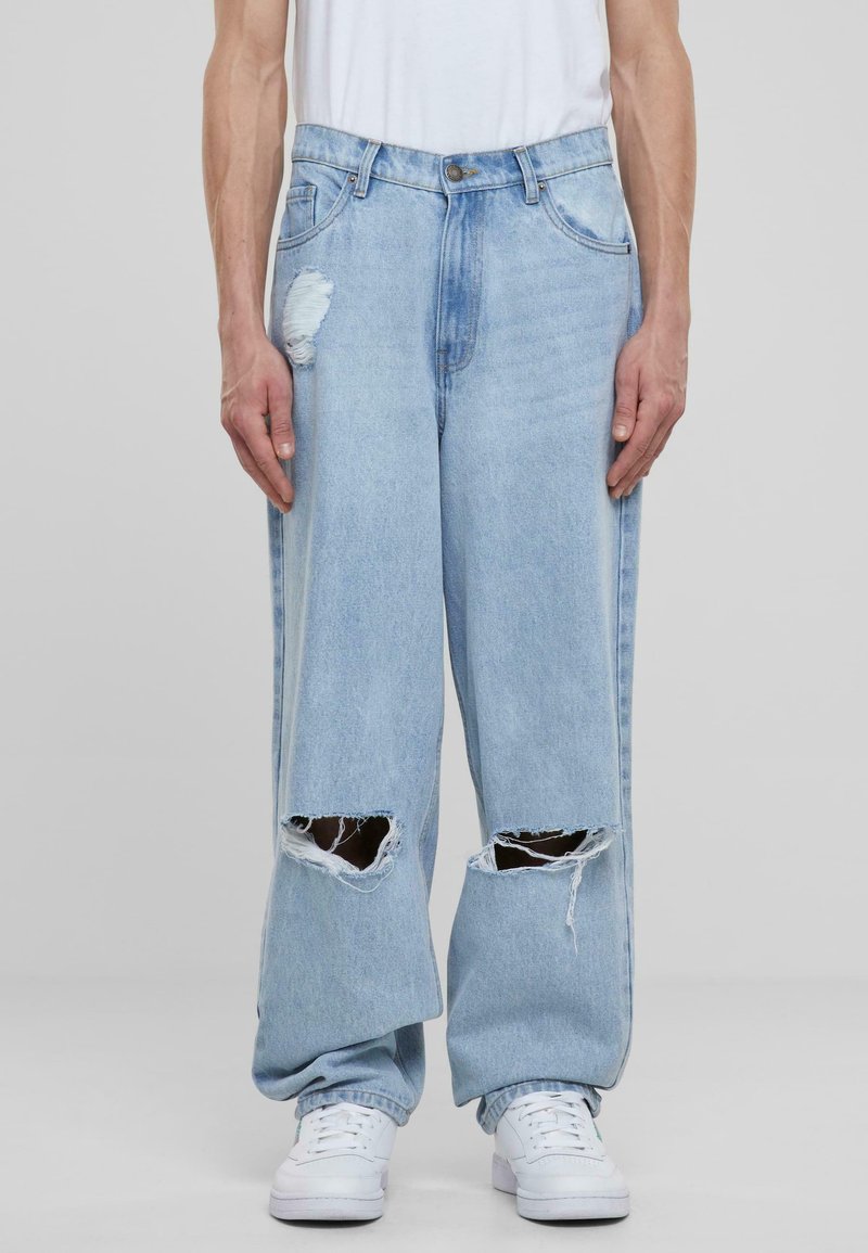 Jeans de color azul claro, rasgados y de corte holgado, con grandes cortes en las rodillas, un desgastado sutil y un diseño clásico de cinco bolsillos.