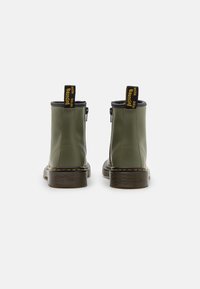 Botas de tobillo verdes con un acabado suave, presentan un zipper lateral, costuras blancas y un tacón negro. Etiquetas amarillas cosidas en la parte posterior.