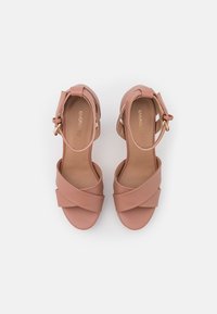Paire de sandales rose poudré à bout ouvert avec des brides croisées et des fermetures à boucle à la cheville sur fond blanc.