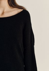 Maglione nero oversize con scollo ampio, realizzato in materiale morbido e soffice. Il tessuto appare strutturato e caldo, con cuciture delle spalle abbassate.