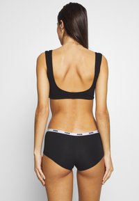 Black sports bra with a low back design, paired with black boyshorts featuring a white Puma logo waistband. Smooth fabric and streamlined shape.