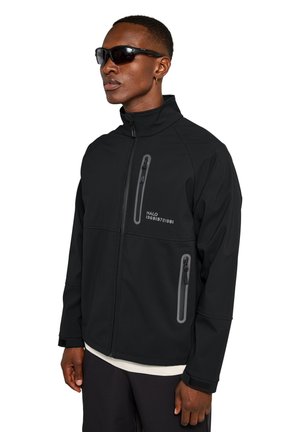 Schwarze Softshelljacke mit hohem Kragen, mit Reißverschluss versehenen Taschen, grauen Akzenten und einer glatten Textur. Verfügt über einen Druck auf der Brust.