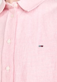 Striped pink collared shirt made of cotton, featuring white buttons and a small logo with red, white, and blue accents on the left chest.