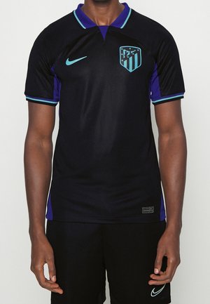 Maillot de football à manches courtes noir et violet avec logo Nike bleu clair et écusson de l'Atletico Madrid porté par une personne, de la nuque à la taille.