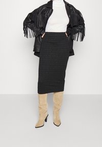 Vrouw in een zwart leren jasje met franjes, een witte coltrui, een zwarte getailleerde midi-jurk en kniehoog beige suède laarzen.
