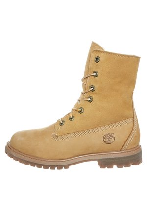 Tan læder støvle med snørebånd, metalhuller, robust gummisål og Timberland trælogo på siden.