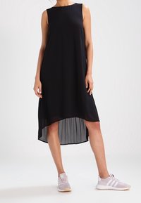 Černé bezramínkové šaty s asymetrickým lemem. Vyrobeny z lehkého materiálu, mají A-čkový střih. V kombinaci se světle růžovými sportovními botami.