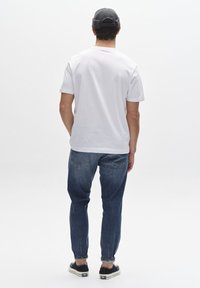 Camiseta blanca de manga corta, vaqueros de mezclilla y zapatillas negras. La camiseta tiene un corte estándar; los vaqueros presentan una pierna estrechada con costuras visibles.
