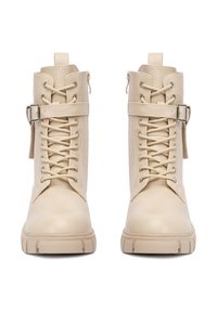 Botine bej cu șireturi, la glezne, cu tălpi masive, catarame pe lateral și tab-uri de prindere, prezentate din față pe un fundal alb.