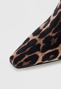 Chaussure à talons hauts en imprimé léopard avec un bout pointu, présentant une texture de tissu doux dans des tons de noir et de marron, et une silhouette élégante.