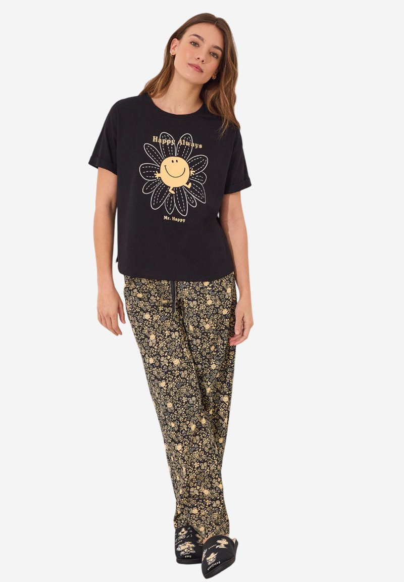 Zwarte t-shirt met gele bloemenafbeelding en tekst "Happy Always" gecombineerd met zwarte bloemenpyjamabroek op een model.