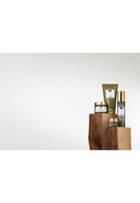 Vier huidverzorgingsproducten in groene en gouden verpakkingen, gerangschikt op een houten display. Bevat crèmetubes, een tube en een pompflacon.