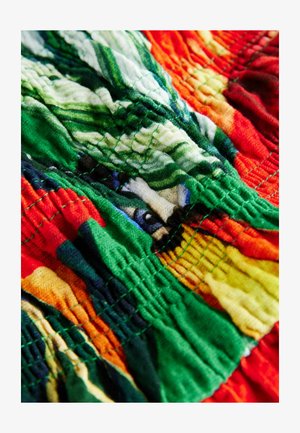 Tissu coloré avec une surface texturée présentant des motifs verts, rouges, jaunes et bleus. Le design comprend des lignes ondulées, cousues, et des plis.