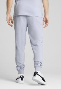 Hellgraue Jogginghose mit elastischem Bund und Bündchen, kombiniert mit schwarz-weißen Turnschuhen. Glatte Textur und lässige Passform.