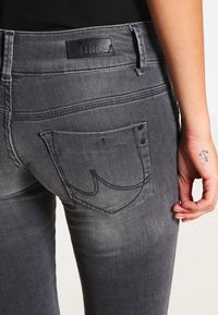 Jeans de mezclilla gris con cintura alta, bolsillos traseros con costuras detalladas y una etiqueta de cuero con la marca "LTB" en la cintura.