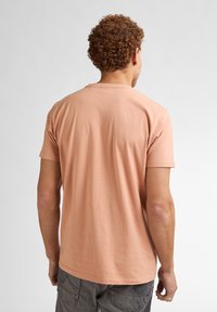 T-shirt a maniche corte con scollo rotondo in morbido cotone pesca, caratterizzato da una vestibilità rilassata, una texture liscia e un design semplice.