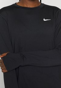 Maglietta atletica nera a maniche lunghe realizzata in tessuto liscio e leggero, con un piccolo logo Nike bianco sul lato sinistro della parte superiore.
