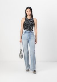 Black sleeveless top with white dot pattern, paired with high-waisted light blue wide-leg jeans and a silver metallic handbag.
