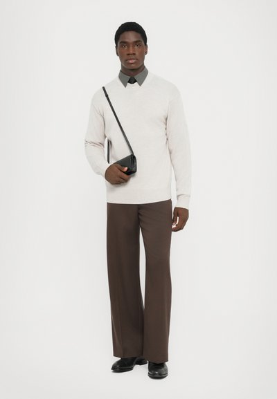 Light grey sweater with v-neck, long sleeves; dark green collared shirt underneath; brown wide-leg trousers; small black shoulder bag; black shoes.