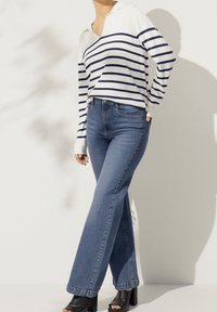 Pullover a righe, bianco e blu navy, con colletto, abbinato a jeans blu svasati e tacchi chunky neri. Texture lisce in tutto.