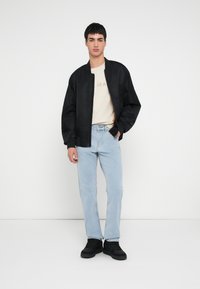 Must mustriga bomberjakk, soonikkoega varrukad, hele beež T-särk tekstiga "JEAN", hele sinised sirge säärega teksad ja mustad kingad.