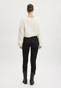 Suéter blanco esponjoso con mangas raglán, combinado con jeans ajustados negros y botas de cuero marrón hasta la rodilla con acentos metálicos.