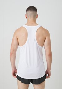 Hvid ærmeløs tanktop med brede armhulninger og et glat, let materiale. Båret med sorte shorts. Minimalistisk design, ingen synlig branding.