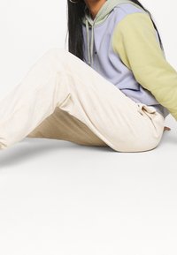 Ljust beige kordtöjbyxor med en texturerad finish, i kombination med en tvåfärgad huvtröja i pastell-lila och grön. Avspänd passform och dragsko-detalj.