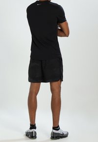 Svart kortärmad Nike träningsskjorta med en reflekterande logga, parat med svarta mönstrade shorts och svarta sneakers med vita accenter.