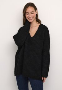 Maglione nero a coste con scollatura a V profonda, vestibilità oversized e maniche lunghe. Tessuto a maglia con un aspetto morbido e peloso. Abbinato a jeans blu scuro.