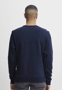 Navy blue sweatshirt with long sleeves, ribbed neckline, and cuffs. Smooth texture and simple design with no visible logos or patterns.