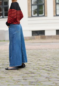 Top de manga larga a rayas rojas y negras, combinado con pantalones vaqueros azules de pierna ancha, ambos mostrando un ajuste casual y relajado con una textura sólida.