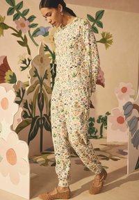 Set di abbigliamento da casa con stampa floreale caratterizzato da colori pastello su tessuto morbido, composto da una maglietta e pantaloni coordinati. Scarpe marroni con texture completano l'outfit.
