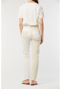 T-shirt blanc et jeans couleur crème vus de l'arrière. Les jeans disposent de deux poches arrière avec un motif subtil. Silhouette ajustée et élégante.