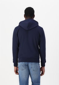Sweat à capuche en coton bleu marine avec une texture douce, poche kangourou et une capuche spacieuse. Coupe ajustée associée à un jean bleu clair.