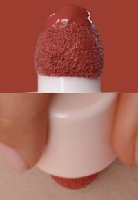 Color de labios líquido en un aplicador redondo con punta difusa, en un tono marrón rojizo intenso, aplicado sobre la piel. Textura suave, acabado mate.