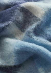 Textureret uldstof i forskellige nuancer af blå, der har bløde, fluffy fibre med et mønster af lysere og mørkere toner.