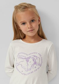 Langärmliges cremefarbenes Shirt mit einem lilafarbenen Grafikmotiv von zwei Pferden und dem Text: "Du bist wunderbar, Pferde sind für immer Freunde."