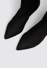 Botas negras de punta afilada hechas de ante con una textura suave, que presentan un diseño elegante y una silueta sofisticada.