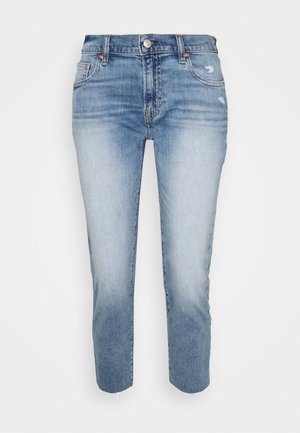 Jeans slim fit blu sbiaditi con leggere abrasioni vicino alle tasche anteriori e orli sfrangiati su uno sfondo bianco.