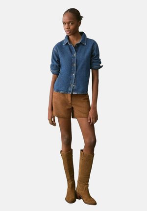 Denim button-up shirt, rolled sleeves, paired with brown suede shorts and knee-high brown boots with a block heel. Smooth texture, casual fit.