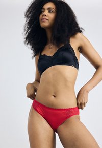 Black lace-trimmed bra and red lace-accented panties. The bra features a smooth fabric, while the panties have a soft texture and scalloped edges.