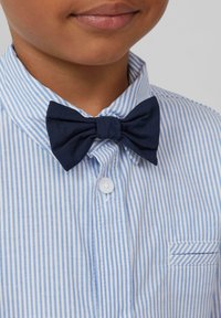 Marineblauwe stoffen vlinderdas met een gestructureerde afwerking, gedragen over een lichtblauwe en witte gestreepte shirt met een button-down kraag en zak.