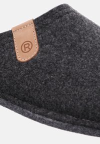 Ciabatta grigia con una forma curvata, caratterizzata da un'etichetta in pelle marrone. La texture è morbida e pelosa, con cuciture visibili.
