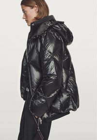 Black puffer jacket with a glossy finish, featuring a hood, zip closure, and side pockets. The design includes quilted sections for insulation.